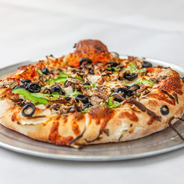 A Home Slice Pizzeria pizza with mushrooms, green peppers, and black olives on a metal pan.