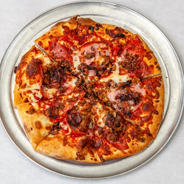 A Home Slice Pizzeria meat lover's pizza, with pepperoni, ham, and sausage, on a metal tray.