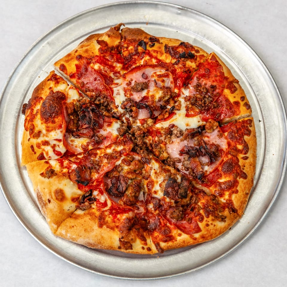 A Home Slice Pizzeria meat lover's pizza, with pepperoni, ham, and sausage, on a metal tray.