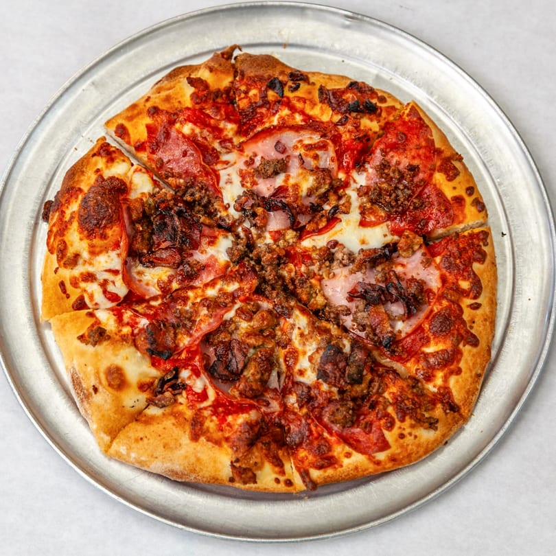 A Home Slice Pizzeria meat lover's pizza, with pepperoni, ham, and sausage, on a metal tray.