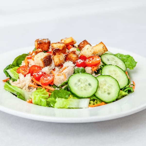 A fresh Home Slice Pizzeria salad with lettuce, cucumbers, tomatoes, croutons, and shredded cheese.