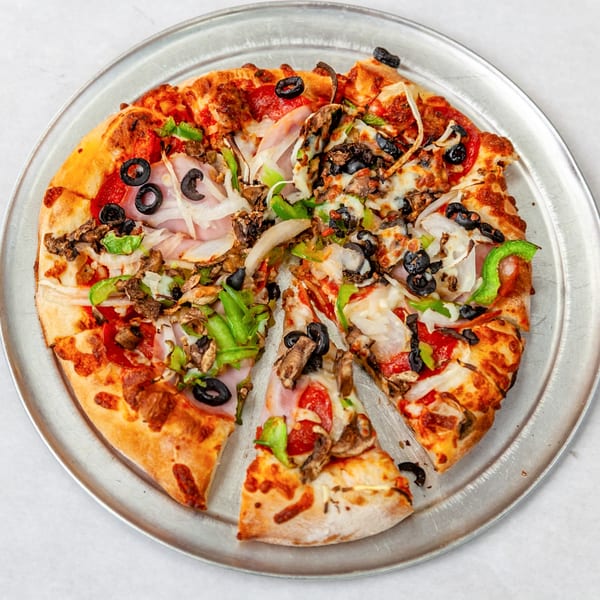 A Home Slice Pizzeria pizza with various toppings, including olives, peppers, and onions, on a metal tray.