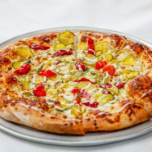 Home Slice Pizzeria's pizza with pickles, red peppers, and white sauce on a metal tray.