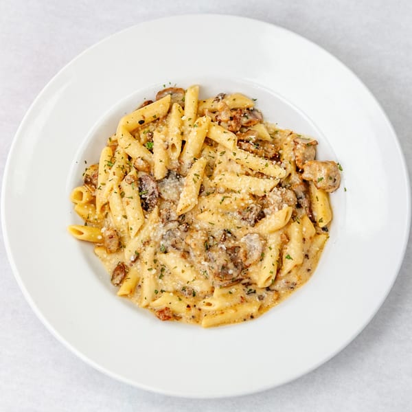 Penne pasta with creamy mushroom sauce, sprinkled with cheese and parsley, served in a white bowl.