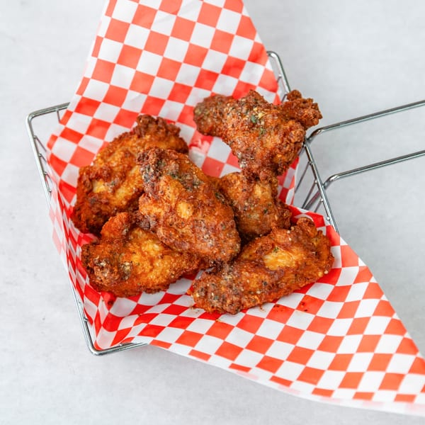 Crispy fried chicken wings in a metal basket lined with red and white checkered paper.